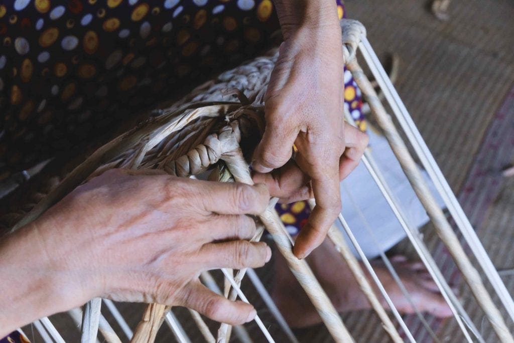 Artisan hands binding natural fiber strips onto a metal frame in Vietnam.