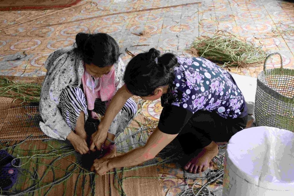 Two Viet Trang artisans weaving seagrass by hand in Vietnam.
