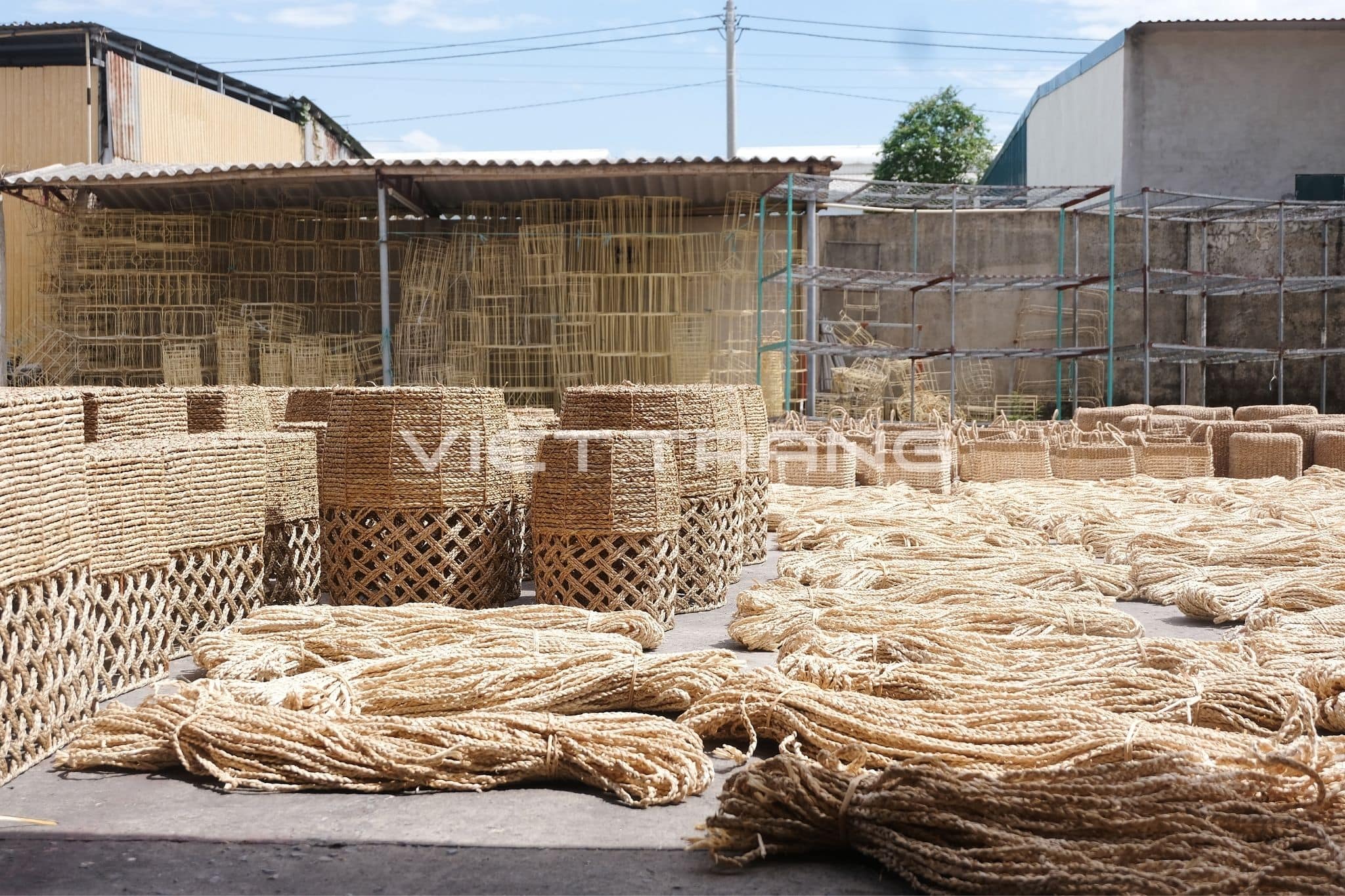 Factory yard in Vietnam with stacked woven baskets and seagrass rope drying in the sun.