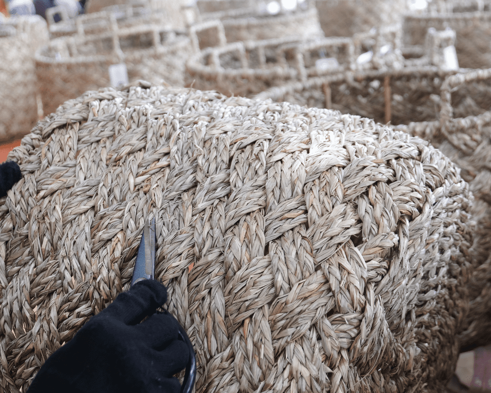 Artisan trimming loose fibers from a woven pouf during finishing in Vietnam.