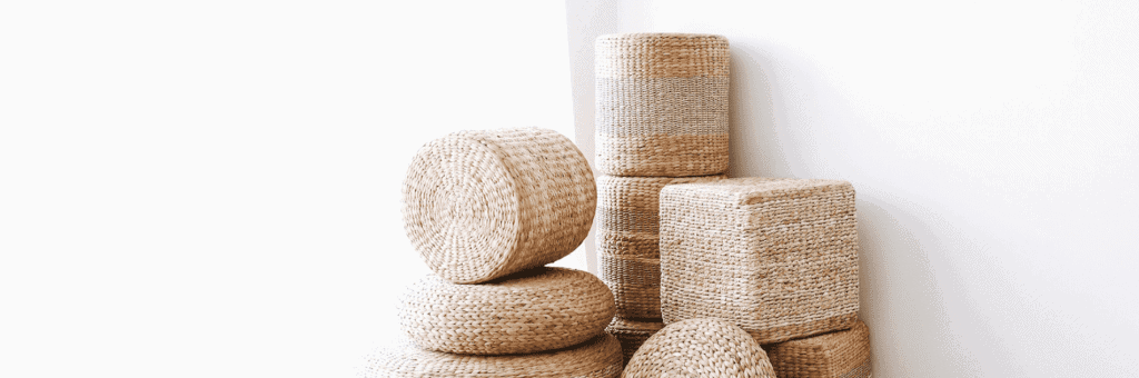 Stacked woven poufs and cushions in natural fiber tones, handmade in Vietnam.